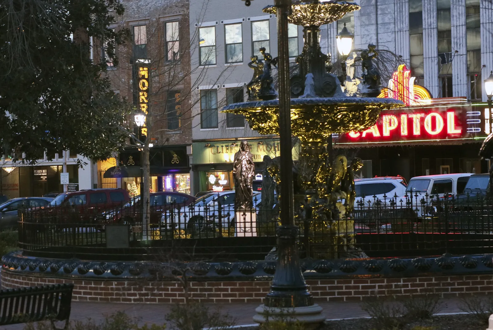 The fountain in Fountain Square Park at dusk, with The Capitol's lit marquee behind it, in downtown Bowling Green