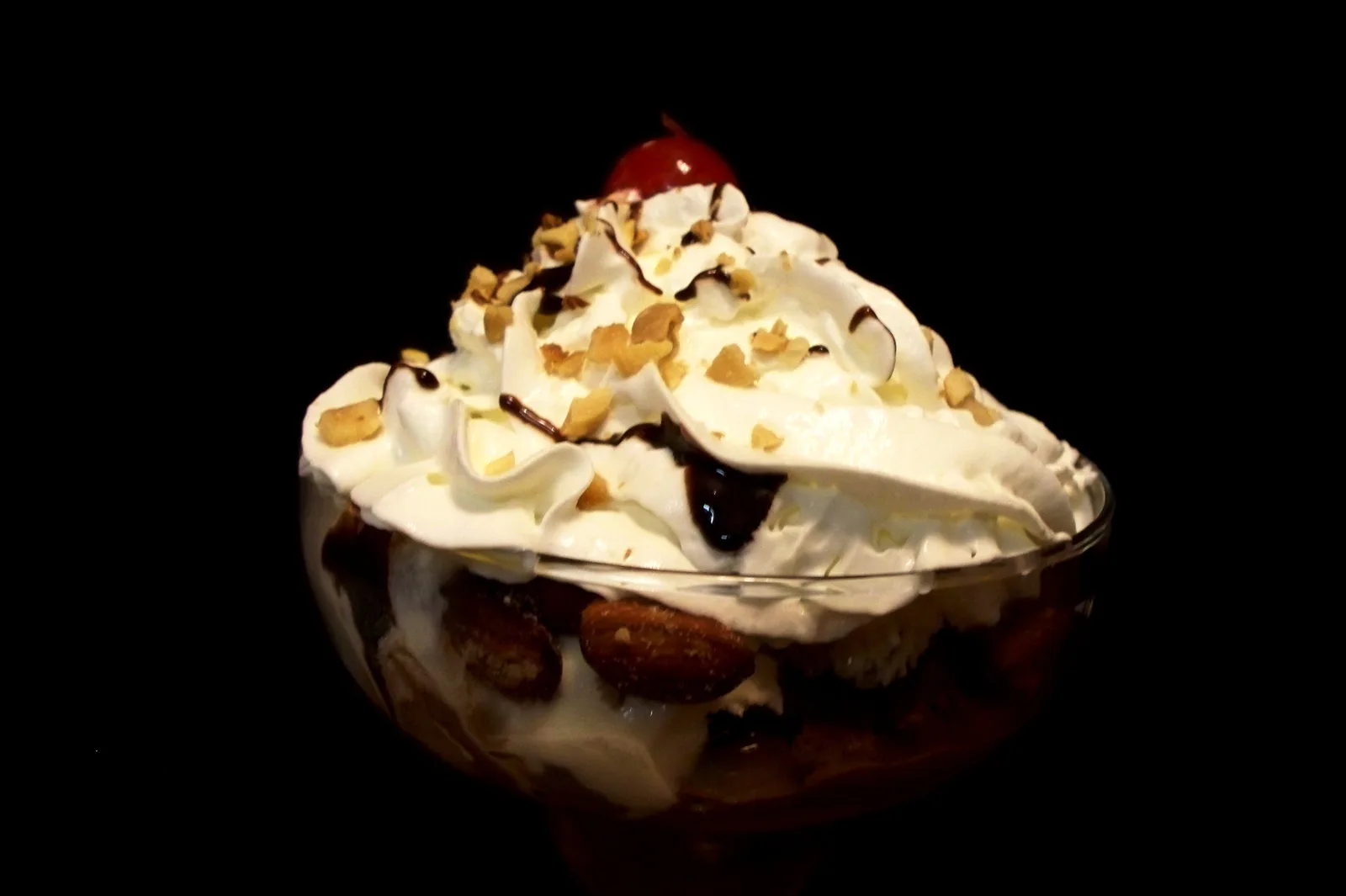 An ice cream sundae with whipped cream, chocolate sauce, nuts and a cherry