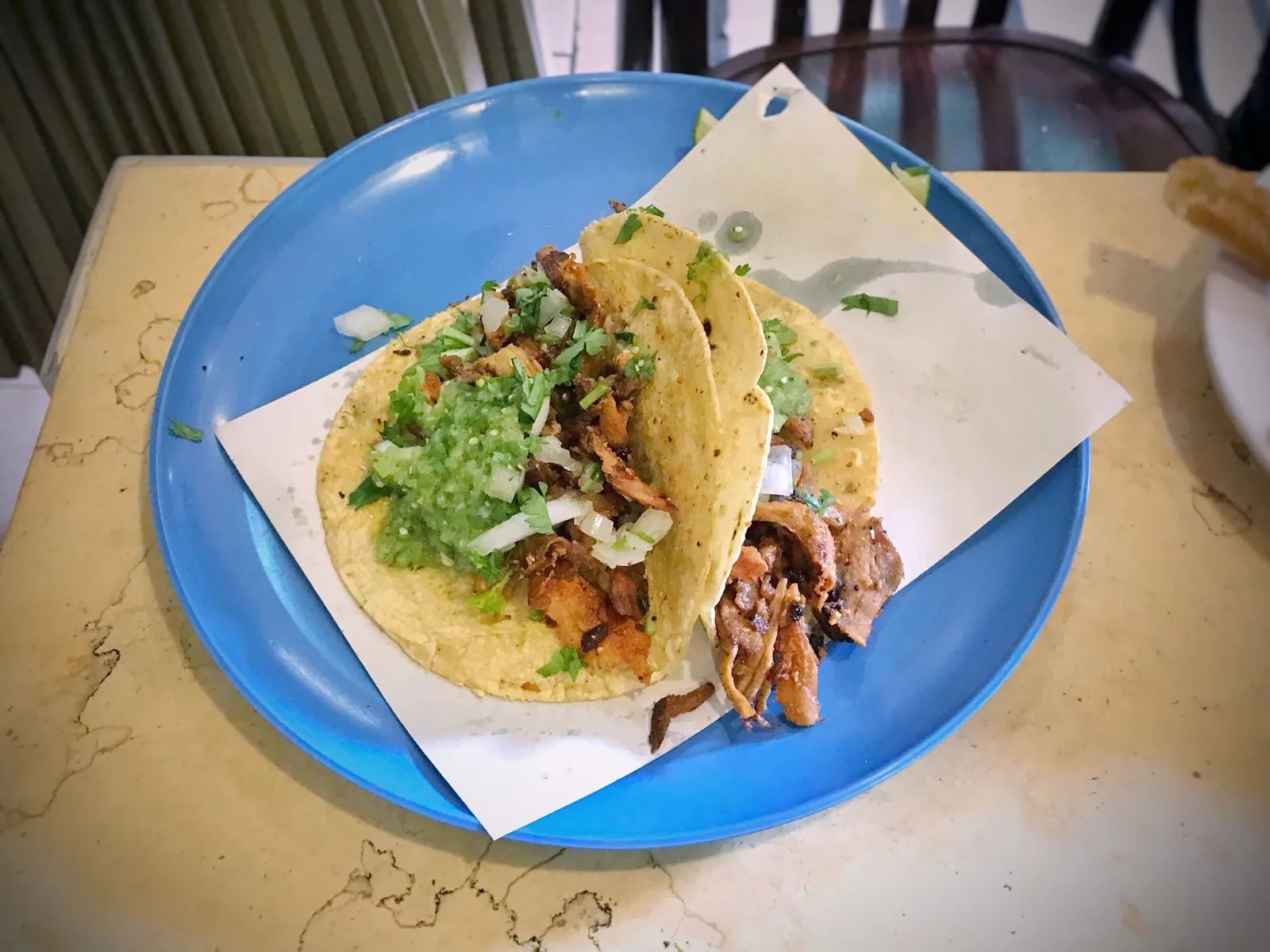 Two al pastor tacos with salsa verde, onion and cilantro on a blue plate