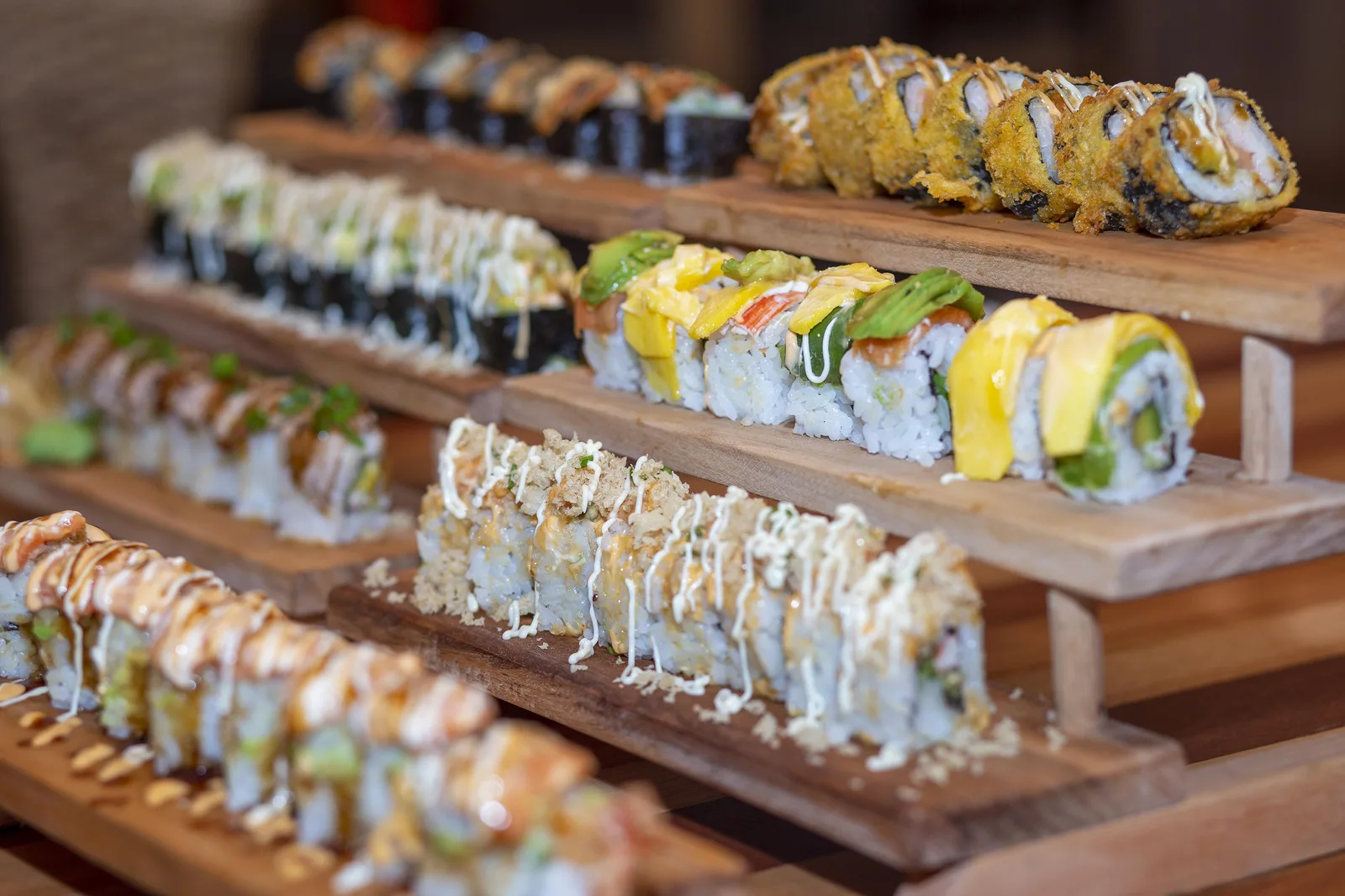 Rows of specialty sushi rolls on tiered wooden serving boards
