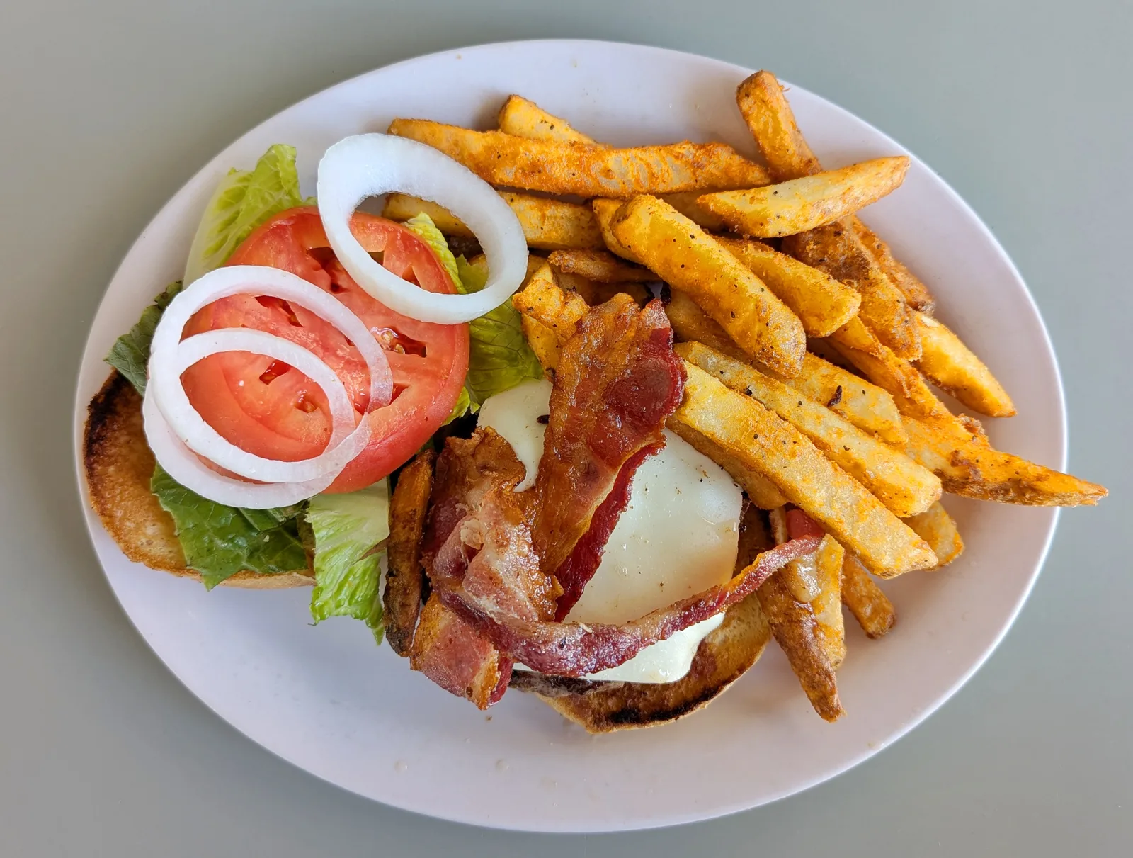 A bacon cheeseburger with lettuce, tomato, onion and seasoned fries at a diner